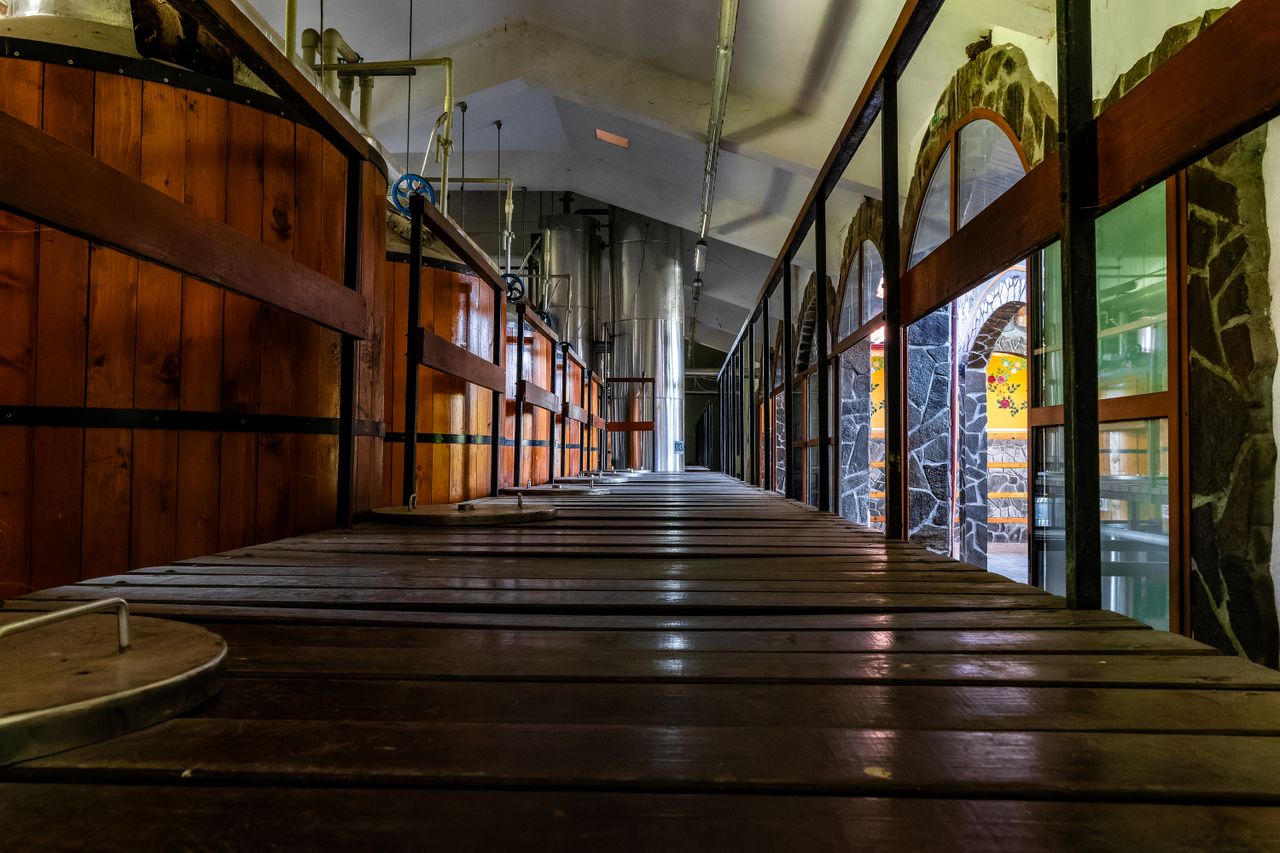 services-img Wide-angle view of a rustic brewery interior showcasing wooden fermentation tanks and industrial brewing equipment.