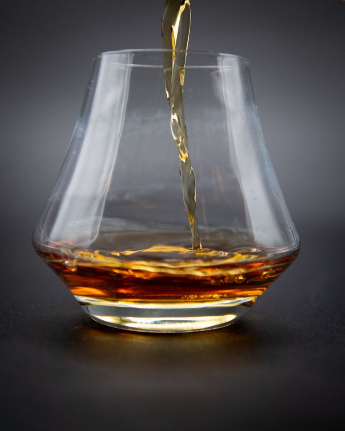 about-img A close-up shot of whiskey being poured into a glass, showcasing rich amber hues.